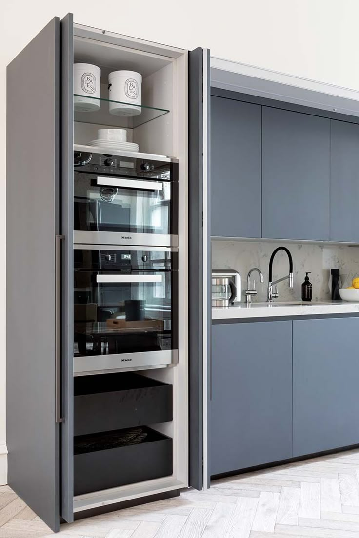 an open cabinet in the middle of a kitchen with grey cabinets and white counter tops