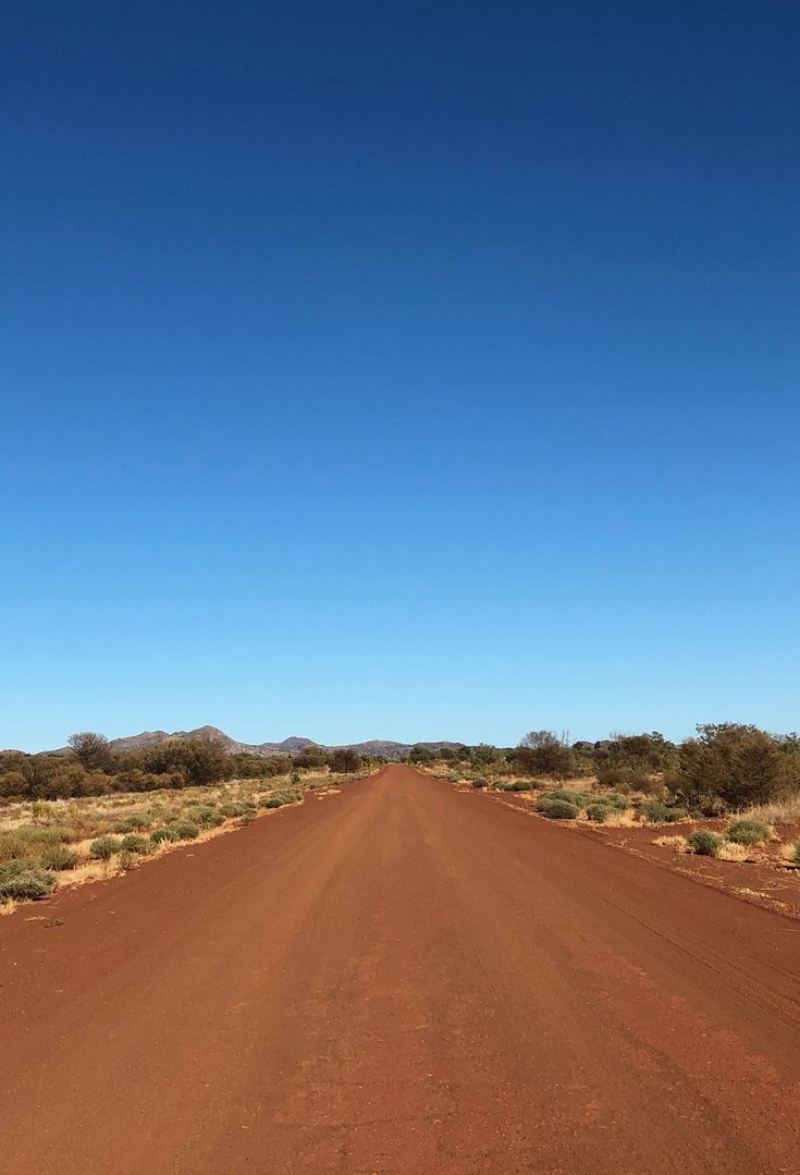 an empty dirt road in the outback with no cars on it's sides