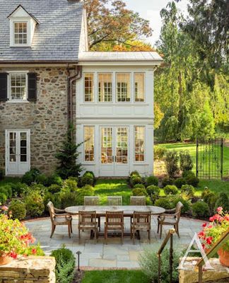 a large white house surrounded by lush green trees and flowers in front of it is an outdoor dining area