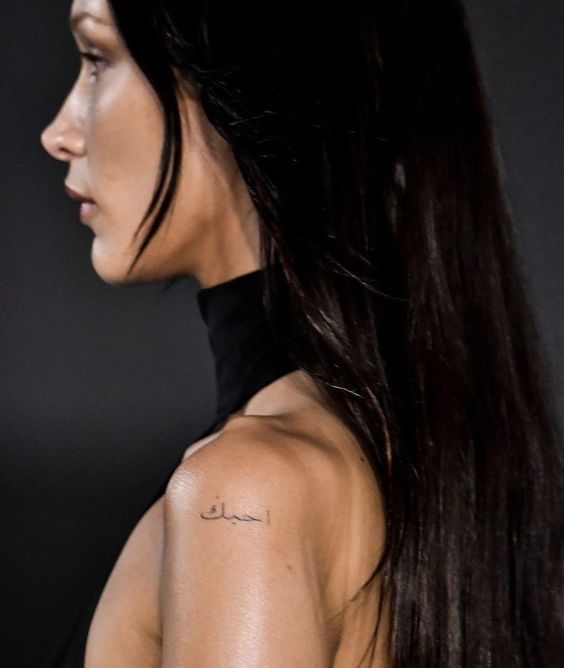 the back of a woman's shoulder with arabic writing on her left upper arm