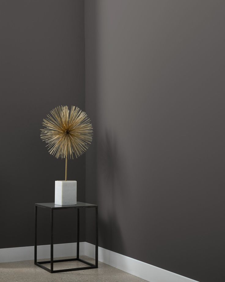 a small table with a vase on it in front of a gray wall and floor