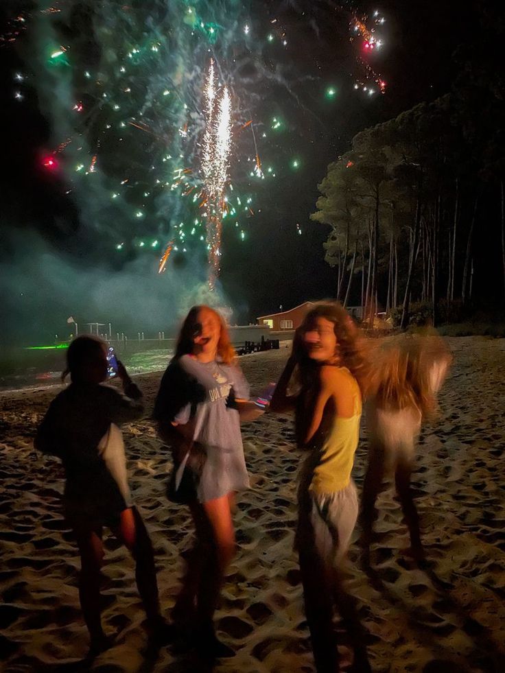 three girls standing on the beach with fireworks in the background