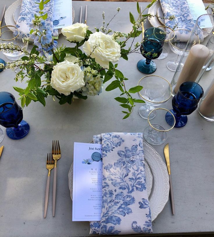 the table is set with blue and white plates, napkins, silverware, and flowers