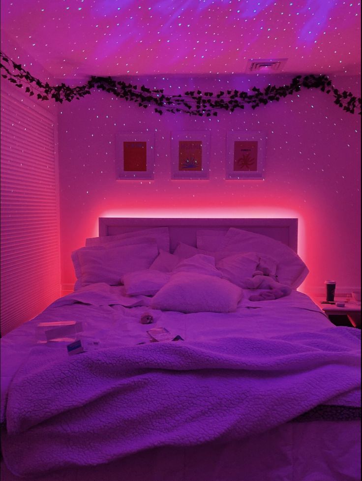 a bed in a room with purple lights on the ceiling and white linens all over it