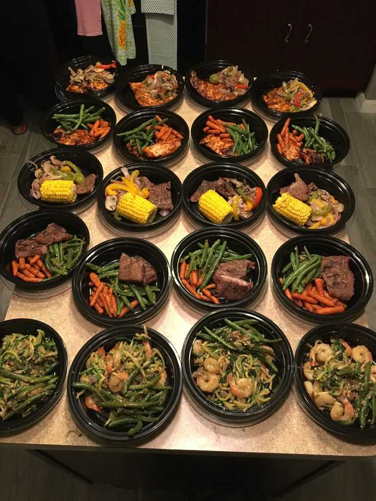 a table topped with lots of black plates filled with different types of food and veggies