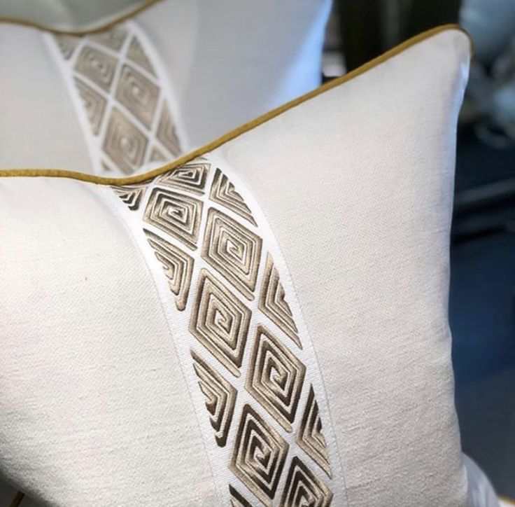 two white pillows with gold trim on them