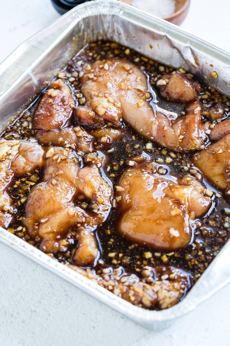 a pan filled with chicken covered in sauce and seasoning on top of a table