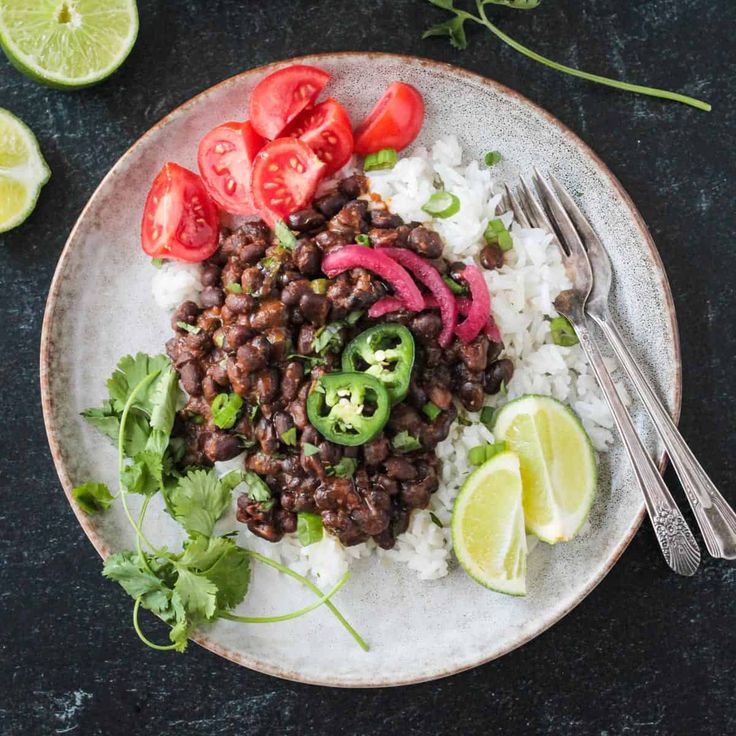 a white plate topped with beans and rice next to sliced limes, tomatoes and cilantro