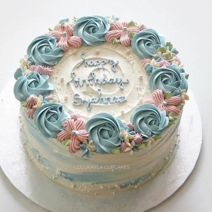 a birthday cake with blue frosting and pink flowers on top is sitting on a white plate