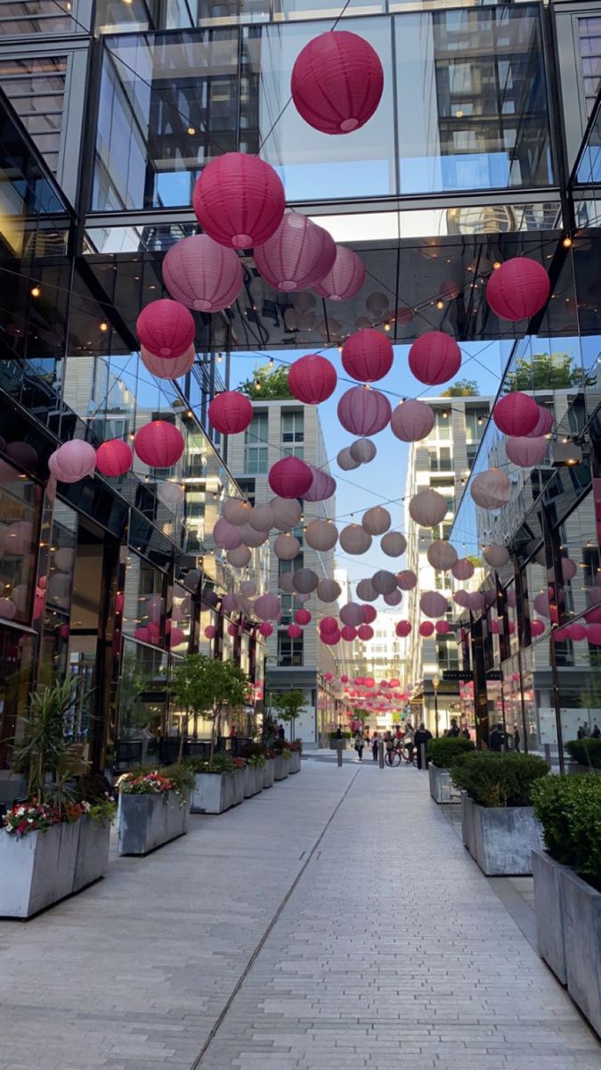 many pink and white lanterns hanging from the ceiling in front of a large glass building