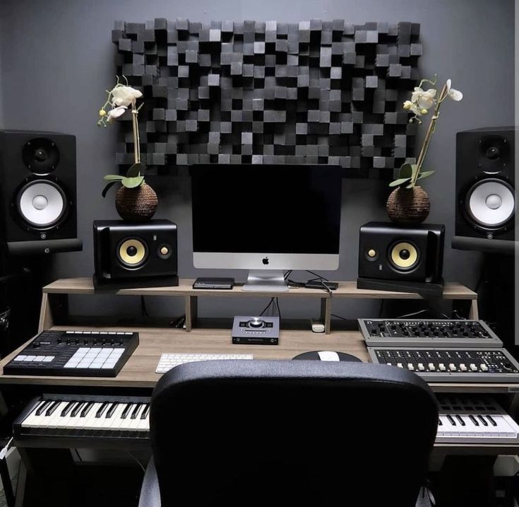 a desk with keyboard, monitor and speakers in front of a wall mounted speaker system