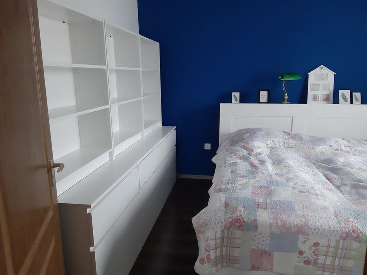 a bedroom with blue walls and white shelving units on the wall next to the bed