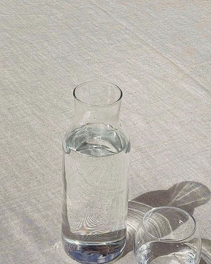 an empty glass with water in it sitting on a tablecloth next to two silver dishes