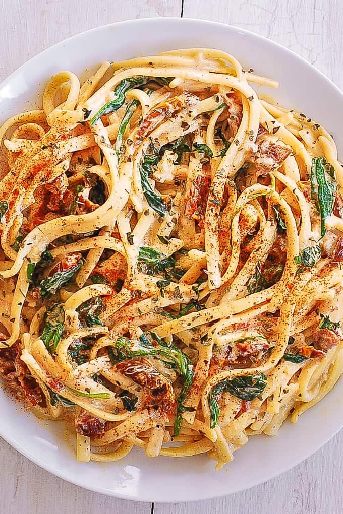 a white plate topped with pasta covered in sauce and spinach leafy toppings