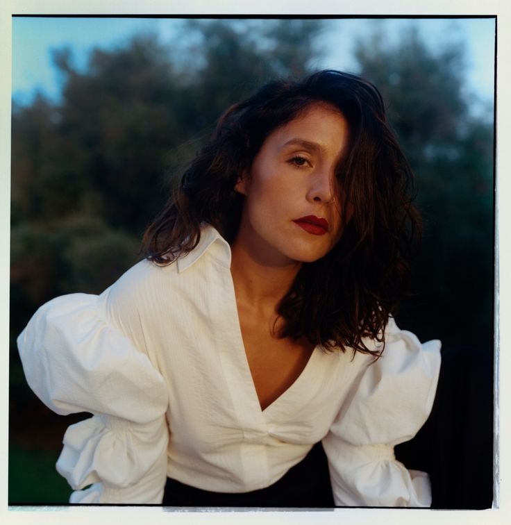 a woman wearing a white shirt and black skirt posing for a photo with trees in the background