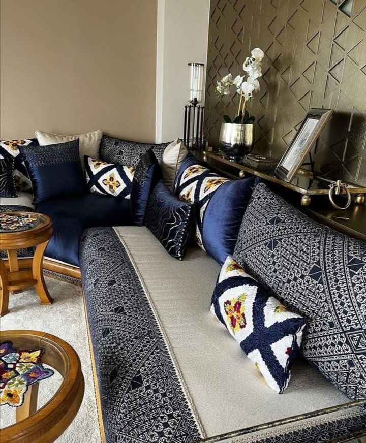 a living room filled with lots of furniture next to a wall covered in gold and blue pillows