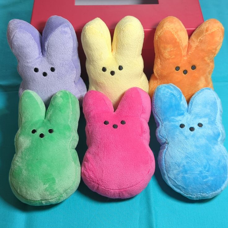 four different colored stuffed animals sitting next to each other on a blue cloth covered table