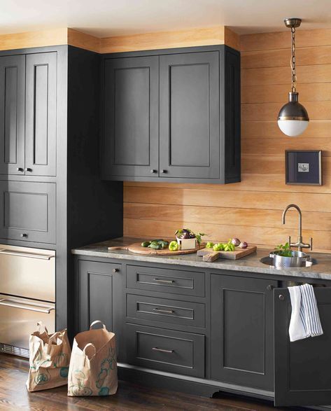 a kitchen with dark gray cabinets and wood paneling on the walls, along with stainless steel appliances