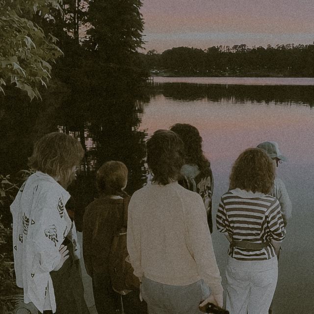 group of people standing next to each other near the water at sunset or sunrise time