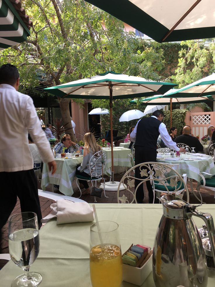 people are sitting at tables with umbrellas and drinks in front of them on a sunny day