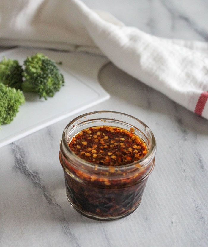 spicy stir fry sauce in a glass jar with broccoli on the side next to it