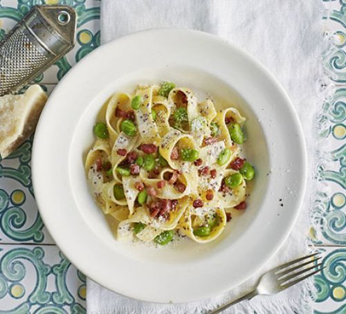 a white bowl filled with pasta and peas on top of a blue and yellow table cloth