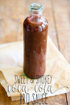 a glass bottle filled with brown liquid sitting on top of a wooden table next to a spoon