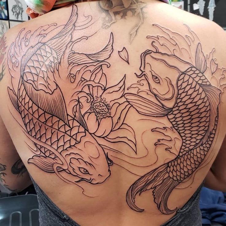 the back of a woman's shoulder with two koi fish and flowers on it