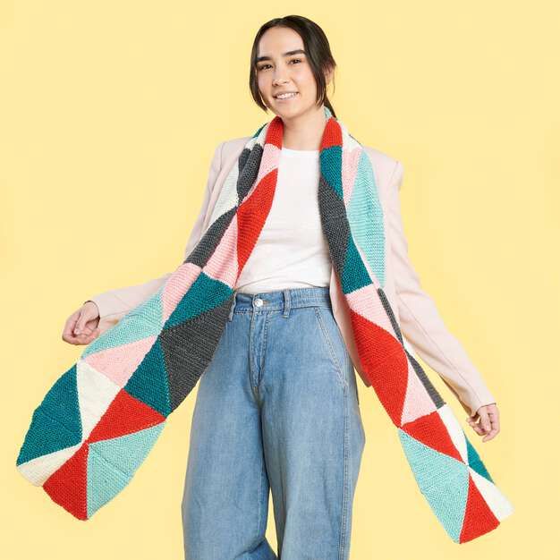 a woman in jeans and a white shirt is holding a multicolored knitted blanket