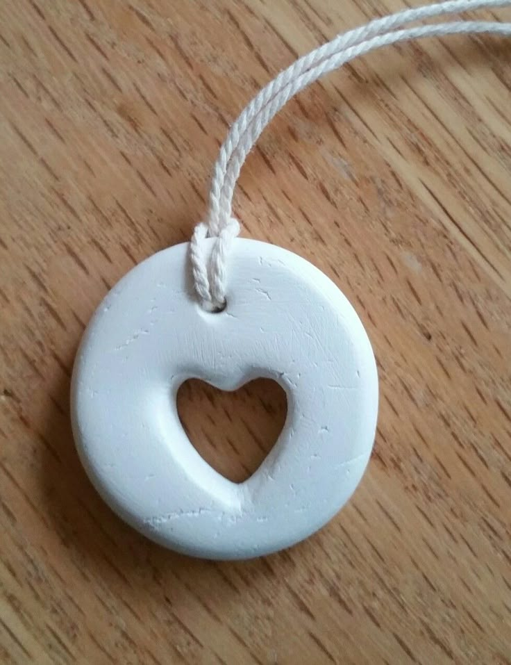 a white ceramic heart ornament hanging from a string on a wooden table top