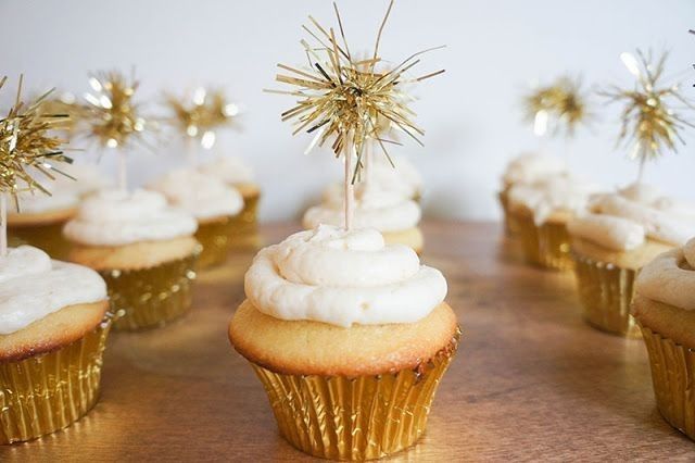 cupcakes with white frosting and gold sprinkles on wooden table