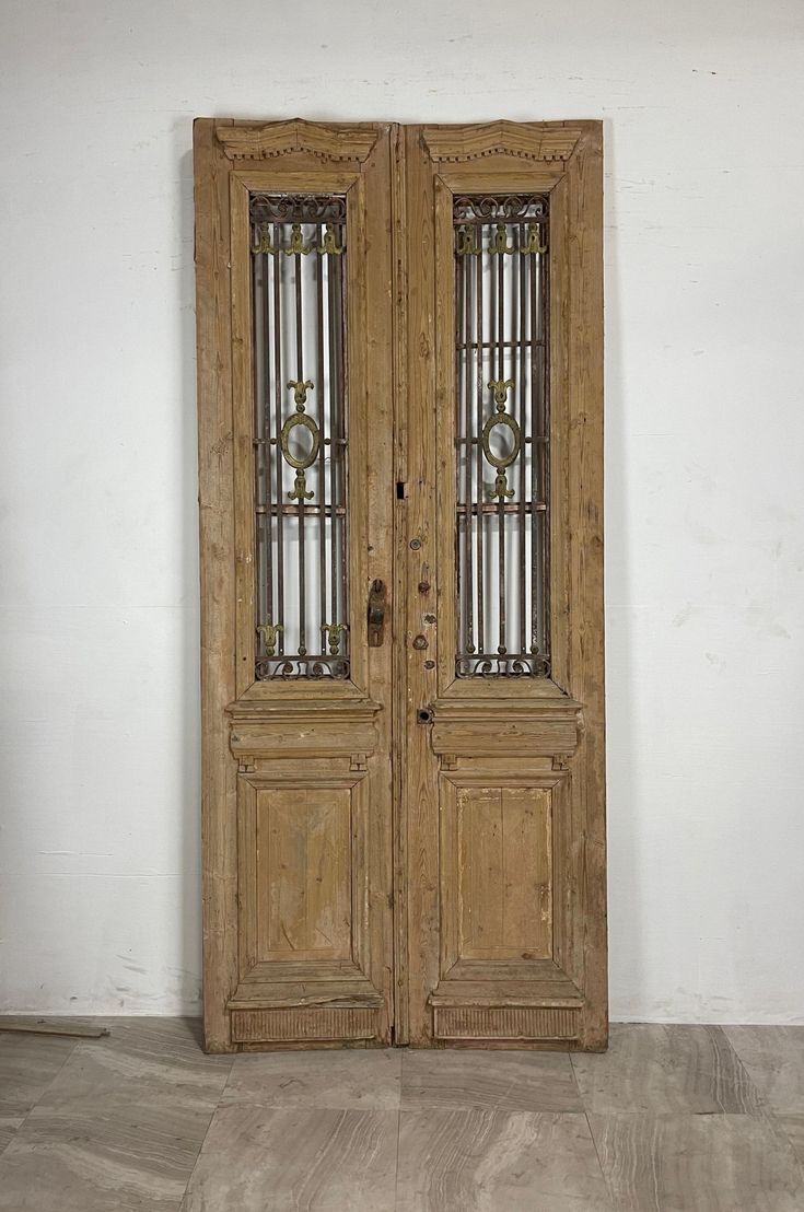 an old wooden double door with glass inserts on the top and bottom panels, in front of a white wall