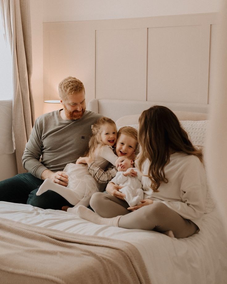 a man, woman and two children are sitting on a bed with their arms around each other