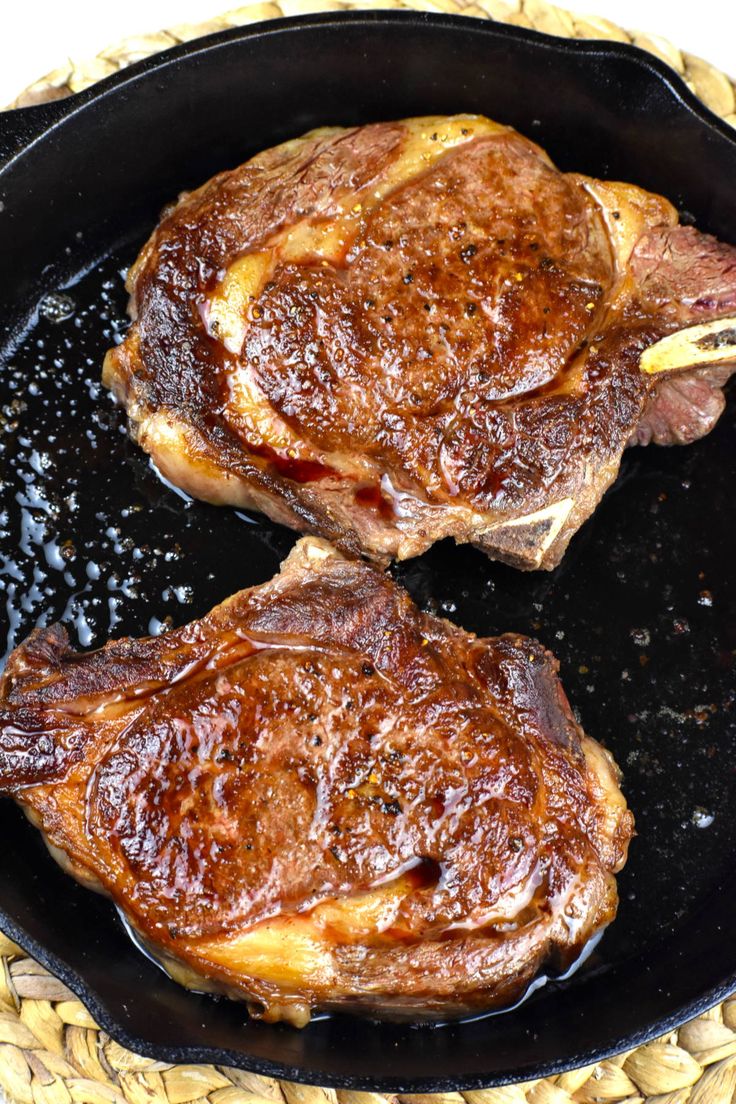 two steaks cooking in a skillet on top of a wicker place mat