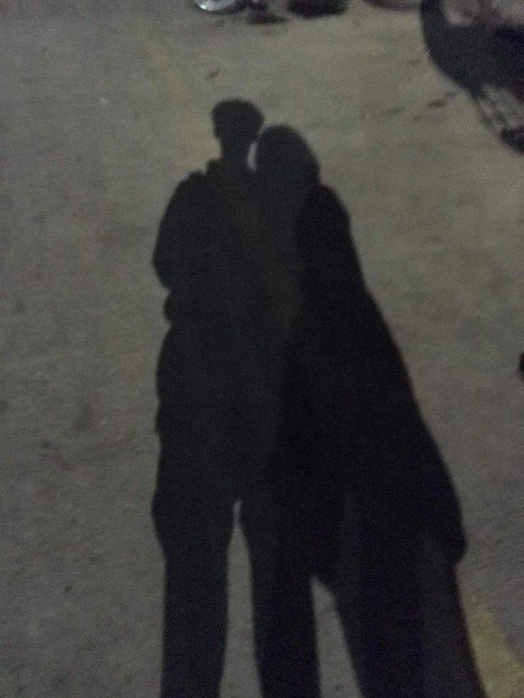 two people standing next to each other in the street with their shadows on the ground