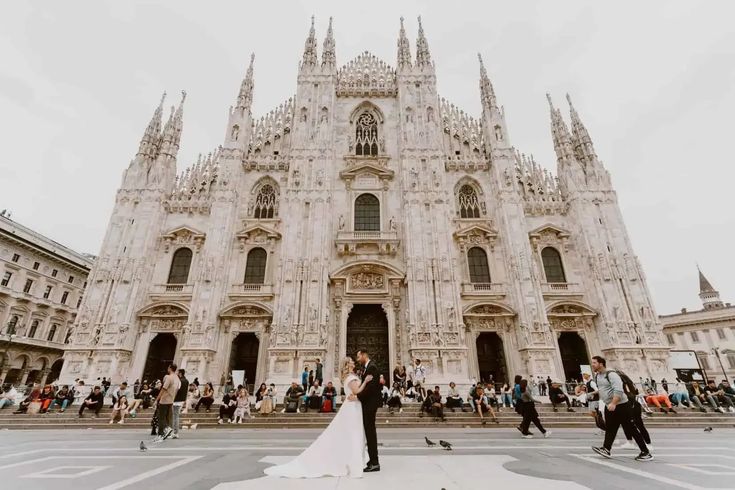 a bride and groom standing in front of a cathedral