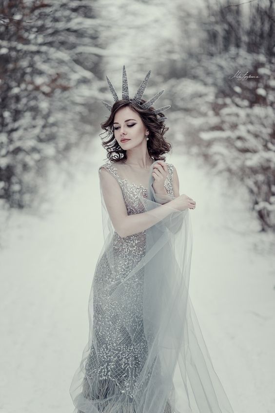 a woman in a dress with horns on her head is standing in the snow wearing a veil