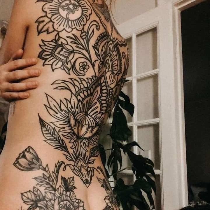 a woman's back with flowers and leaves tattooed on her lower body, in front of a window