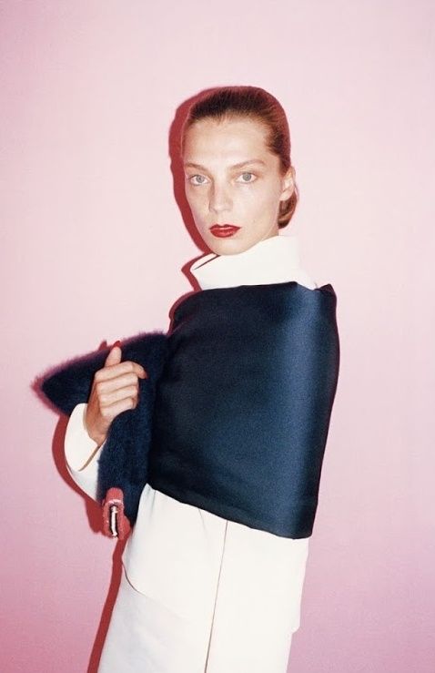 a woman wearing a black and white top with a fur stole around her neck, standing in front of a pink wall