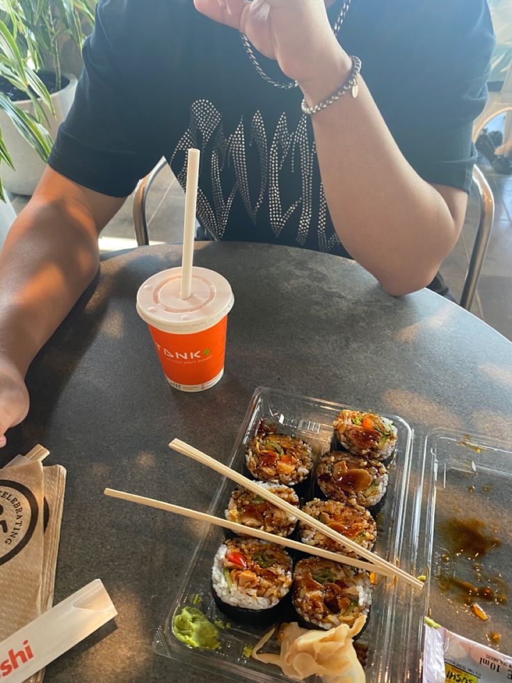 a person sitting at a table with sushi and chopsticks in front of them