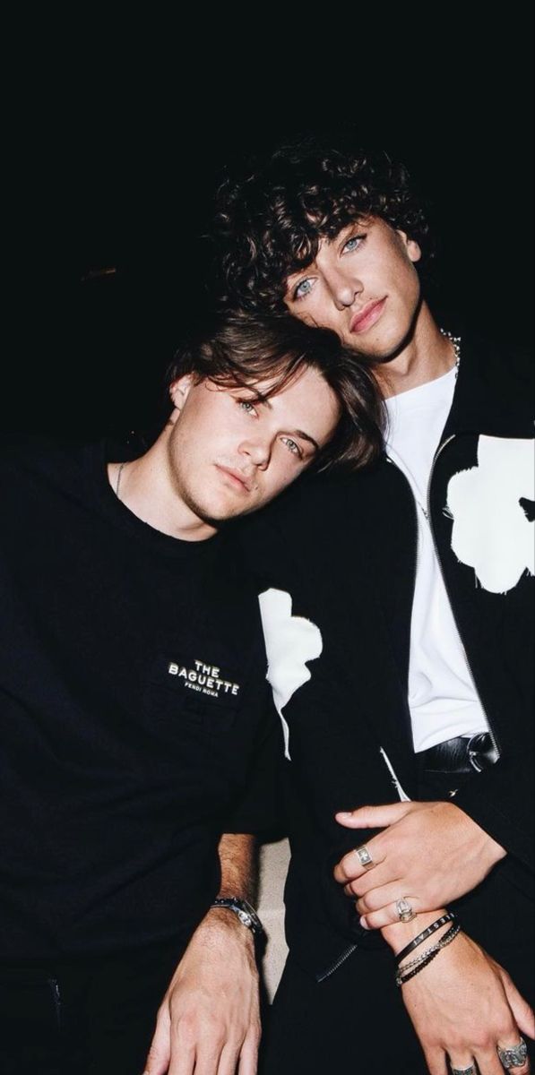 two young men sitting next to each other in front of a black background, one with his arm around the other's shoulder