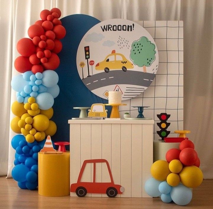 a birthday party with balloons and cars on the wall next to a cake stand that says weoon