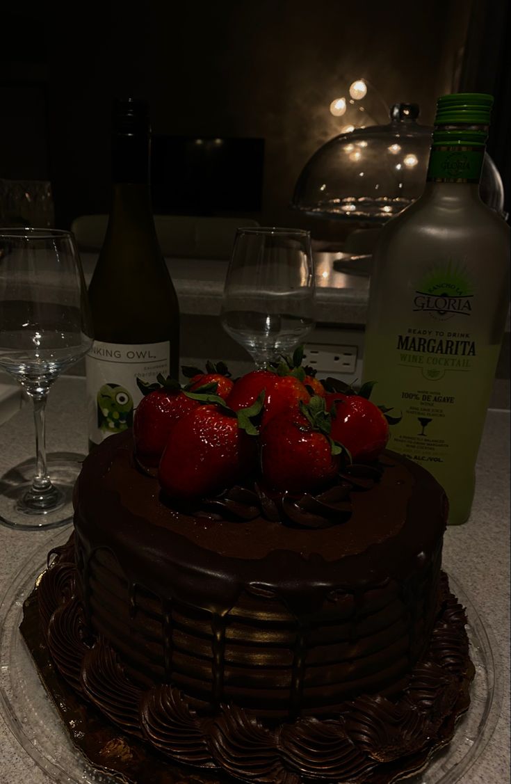 there is a chocolate cake with strawberries on top and wine glasses next to it