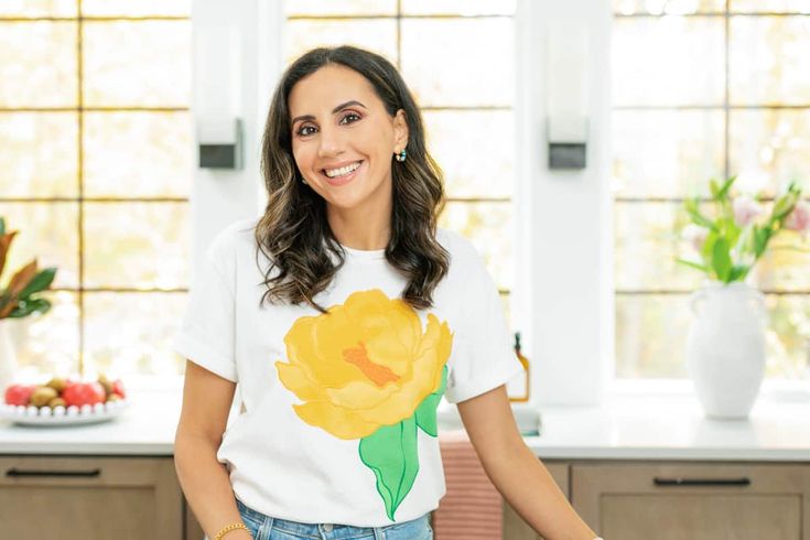 a woman standing in front of a counter top with a yellow flower t - shirt on