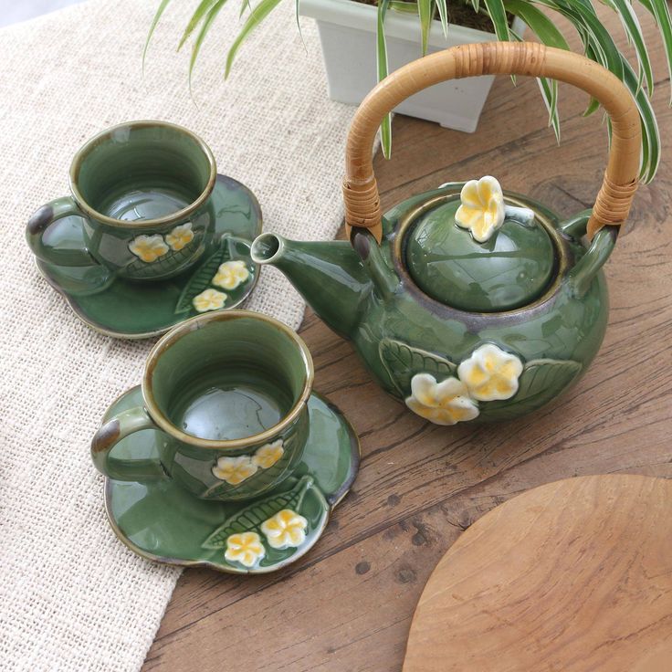 three green teapots with yellow flowers on them sitting next to a potted plant