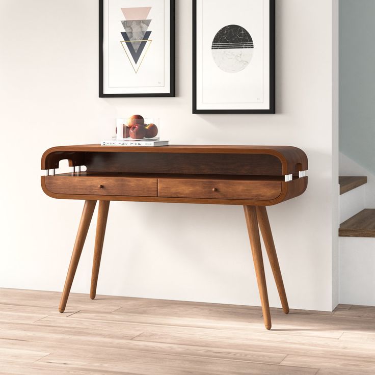 a wooden desk with two framed pictures on the wall above it and below it is a staircase