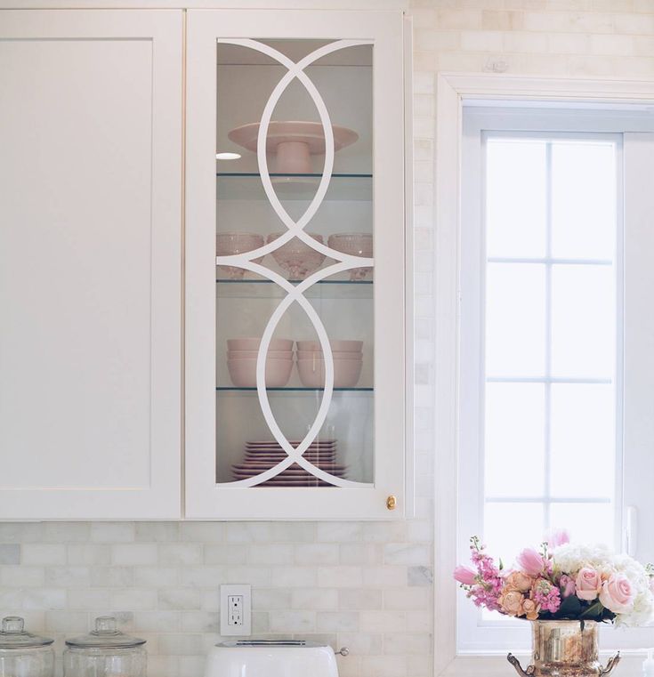 a kitchen with white cabinets and pink flowers