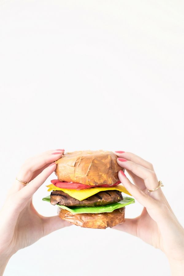 two hands holding up a large hamburger in front of a white background with the burger being held by one hand