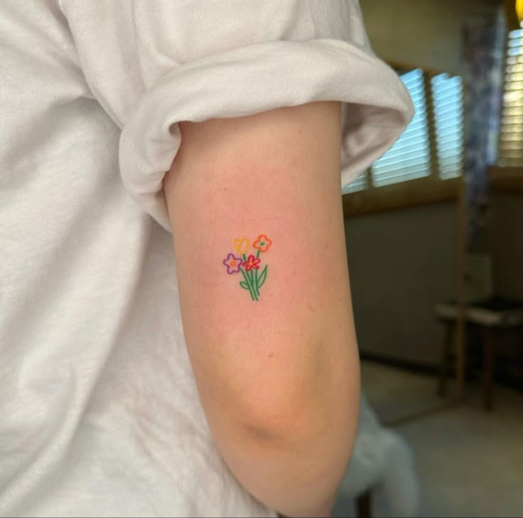 a person with a flower tattoo on their left arm and behind her is a white t - shirt