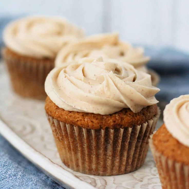 cupcakes with cinnamon butter frosting and cinnamon sticks on a wooden tray next to cinnamon stick